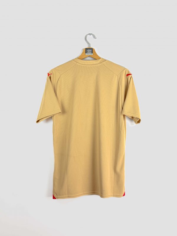Gros plan sur le maillot extérieur authentique du RC Lens 23/24, coloris doré, avec détails du blason sang-et-or et du logo Puma sur le tissu.