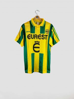 Maillot de football vintage du FC Nantes, domicile saison 1995-1996, bandes verticales vertes et jaunes, sponsor Eurest, logo Adidas et écusson du club sur la poitrine.