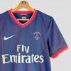 Gros plan sur les fines rayures rouges verticales du maillot PSG 2009-2010, illustrant le design unique de ce maillot rétro du PSG