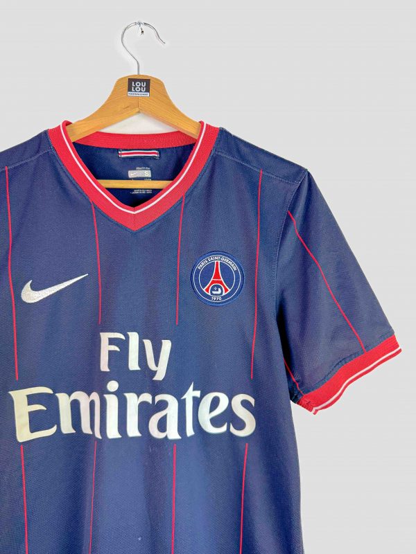 Gros plan sur les fines rayures rouges verticales du maillot PSG 2009-2010, illustrant le design unique de ce maillot rétro du PSG