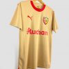 Le maillot away 2023-2024 du RC Lens, de couleur or avec le sponsor Auchan sur la poitrine et l’écusson du club en évidence.