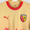 Nouveau maillot extérieur 2023/2024 du RC Lens, arborant un design doré unique avec logo Puma et inscription Auchan, présenté sur cintre.