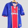 Image d’un maillot de football rétro du PSG datant de 1998. Le maillot domicile est bleu à bande rouge verticale, avec le logo Opel en sponsor central, le signe Nike sur le côté droit de la poitrine et le blason du PSG à gauche. Cette pièce classique des maillots de foot vintage est en très bon état.