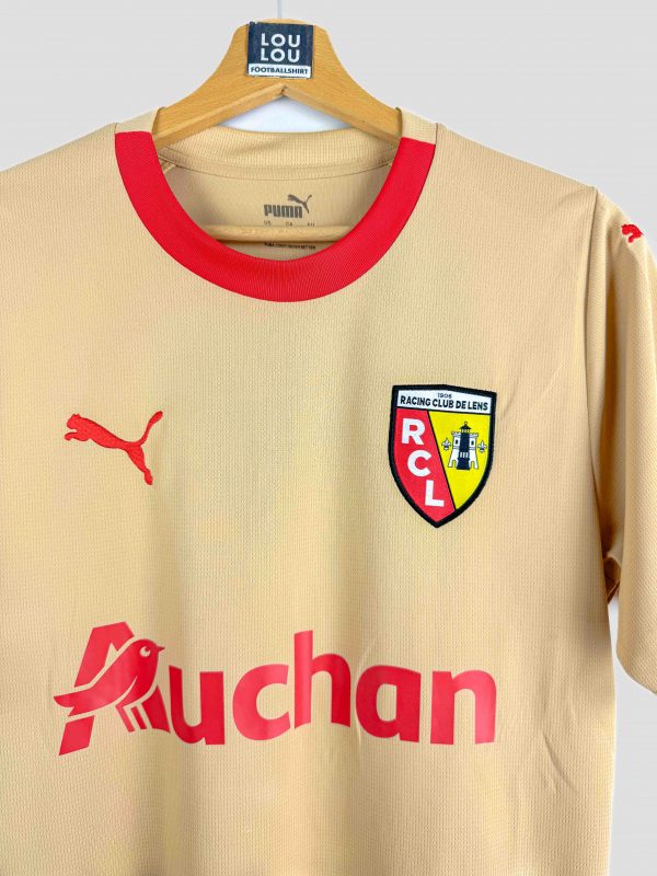 Maillot de football extérieur du RC Lens saison 2023-2024 en version dorée, sponsorisé par Auchan et conçu par Puma, disponible à l’achat.