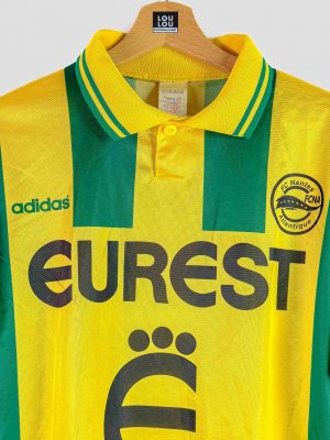 Maillot de football historique du FC Nantes, jaune et vert à rayures verticales, sponsor Eurest au centre, logo Adidas vert et blason du club.